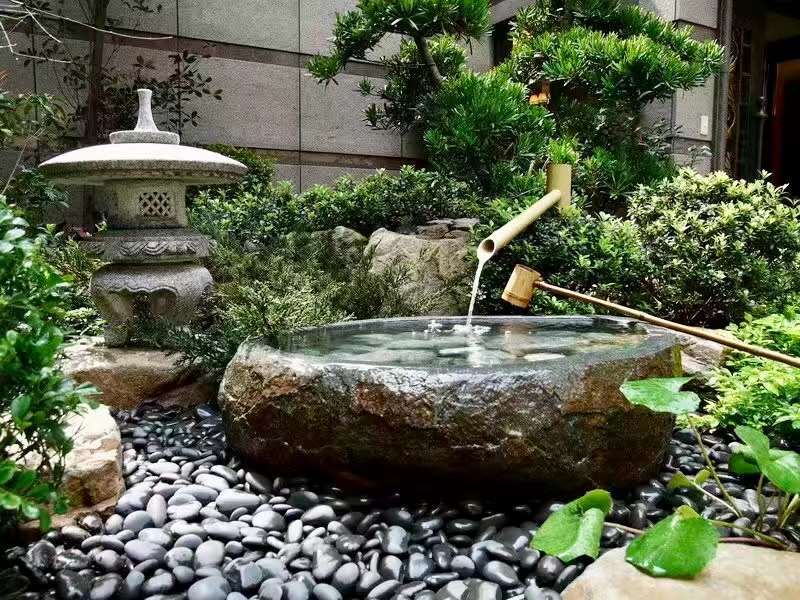 天然黑卵石鋪面搭配景石與地被植物並以竹流水點綴的庭院景觀配置